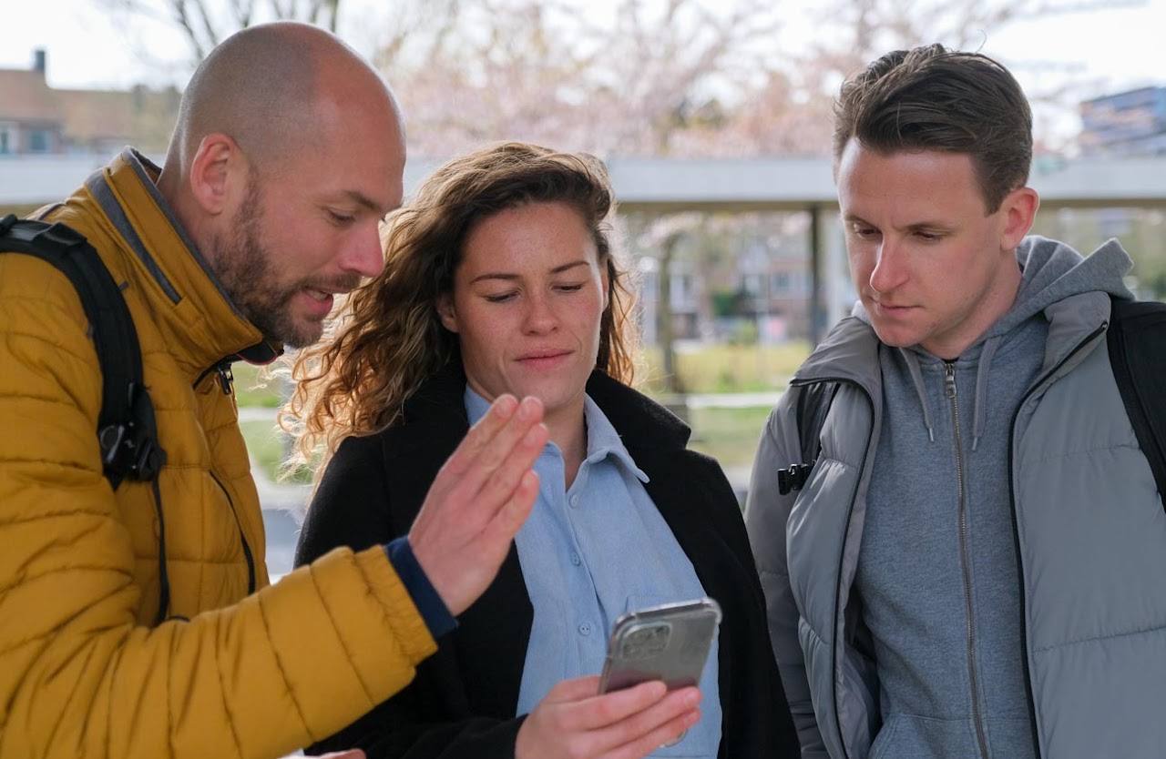 Maarten bekijkt en bespreekt een foto op een smartphone met twee deelnemers