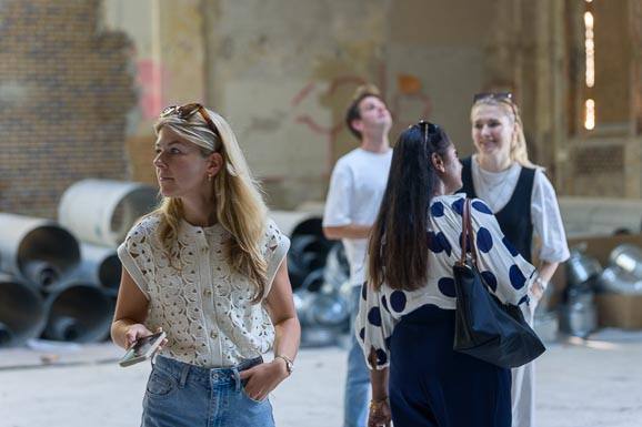 Deelnemers kijken rond in een pand in verbouwing, een van hen met een smartphone in de hand